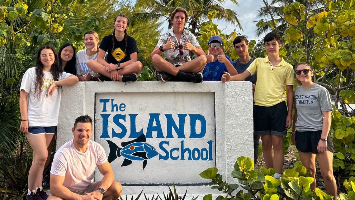 Group of students posed around a stone sign that says The Island School