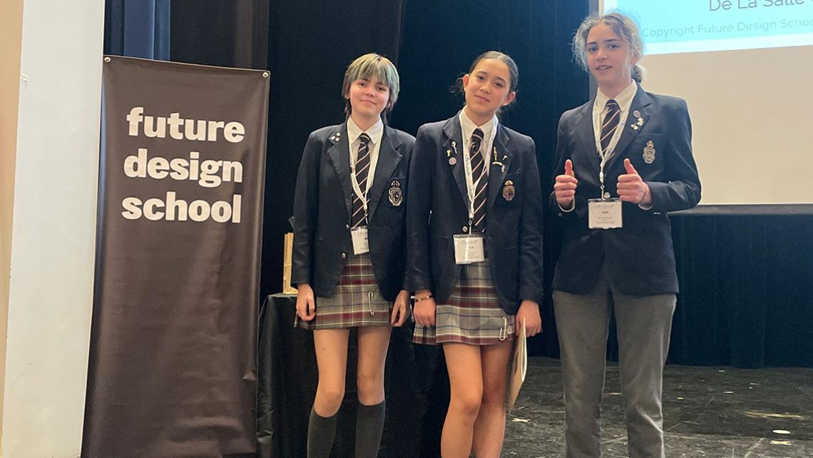 three students stand beside the Future Design Challenge banner