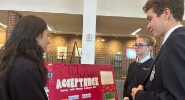 Three students speak in front of display board titled Acceptance