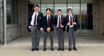 Photo of four students in uniforms standing outside the doors of a school