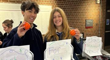 Two students standing behind small basketball hoops marked Shoot for Sustainability