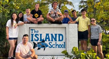 Group of students posed around a stone sign that says The Island School