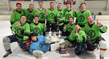 Group oHockey team in green jerseys, posed on the ice with trophy, raising index fingers in number one gesture