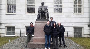 Five students stand around the statue of John Harvard at Harvard University