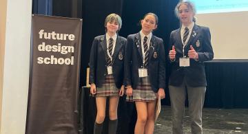 three students stand beside the Future Design Challenge banner