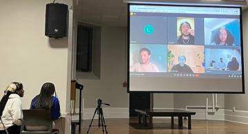 Two students watching speakers on a projection screen